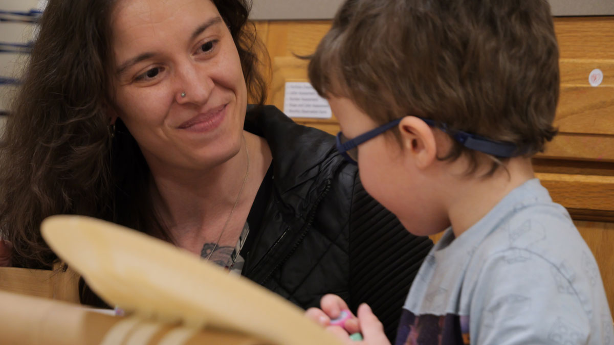 Mother smiling at her young son while he is working on an art project in class.