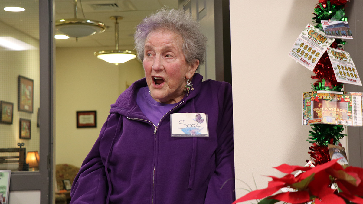 A woman wearing a purple sweater with a name tag on that reads, "Sooz".