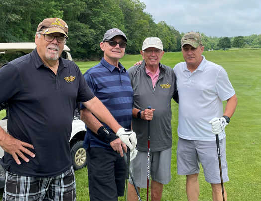 four men stand with golf clubs on a golf green next to a golf buggy