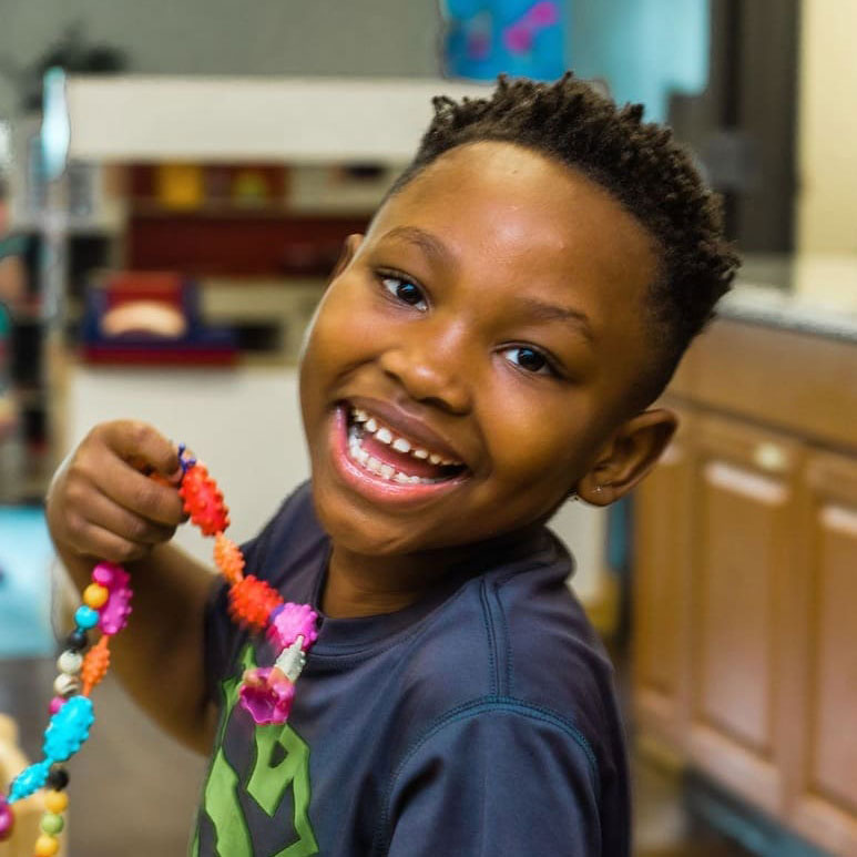 Young boy smiling holding a beaded necklace. 