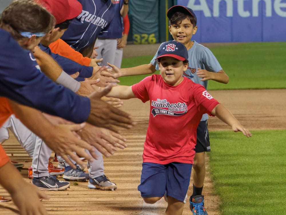 Two boys running the bases and hi fiving players at a Fisher Cats baseball game.