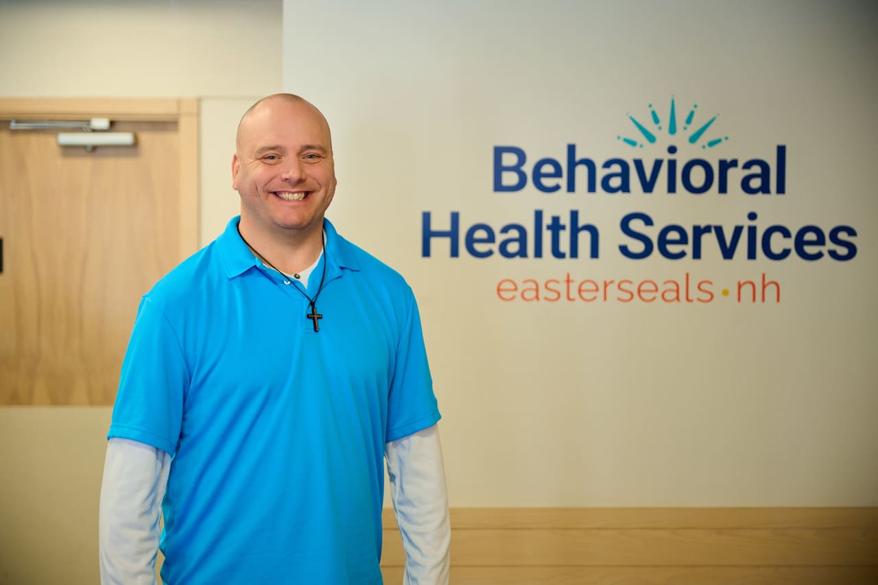Michael Raiche standing to the left of a Behavioral Health Services by Easterseals NH sign